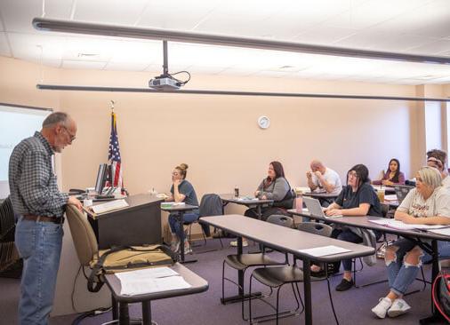 teacher stands in front of rows of students sitting at tables